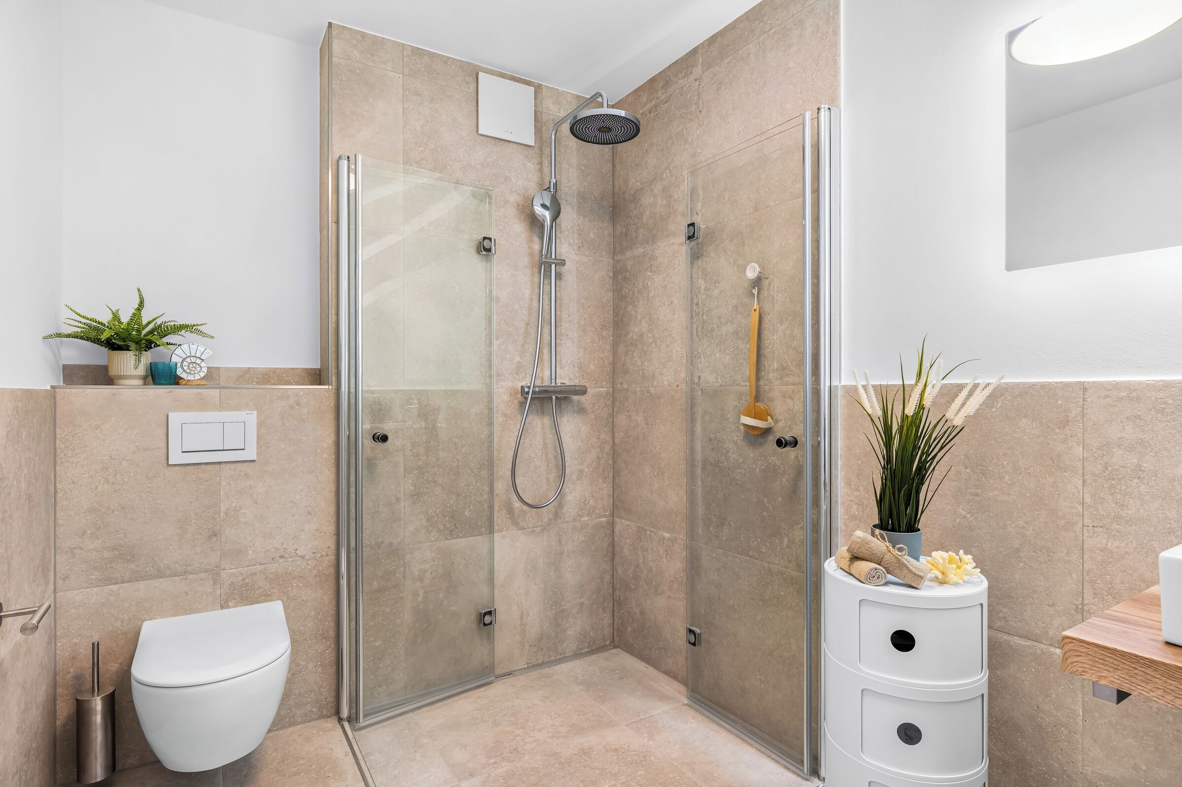 A modern bathroom with a glass-enclosed shower, a toilet, and a small sink with a towel and decorative items.