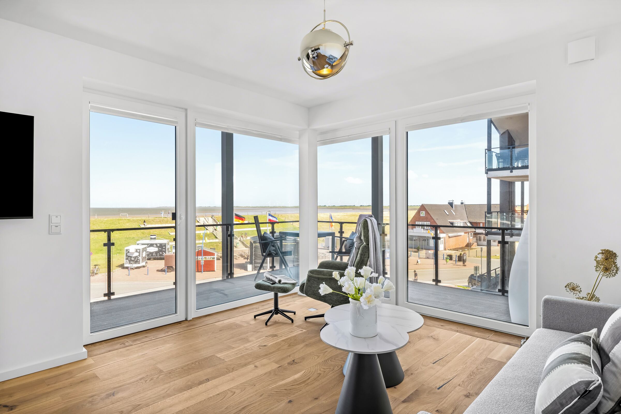 A spacious living room with large windows, a modern chandelier, and a view of the outside.