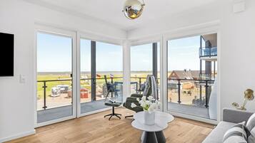 A spacious living room with large windows, a modern chandelier, and a view of the outside.