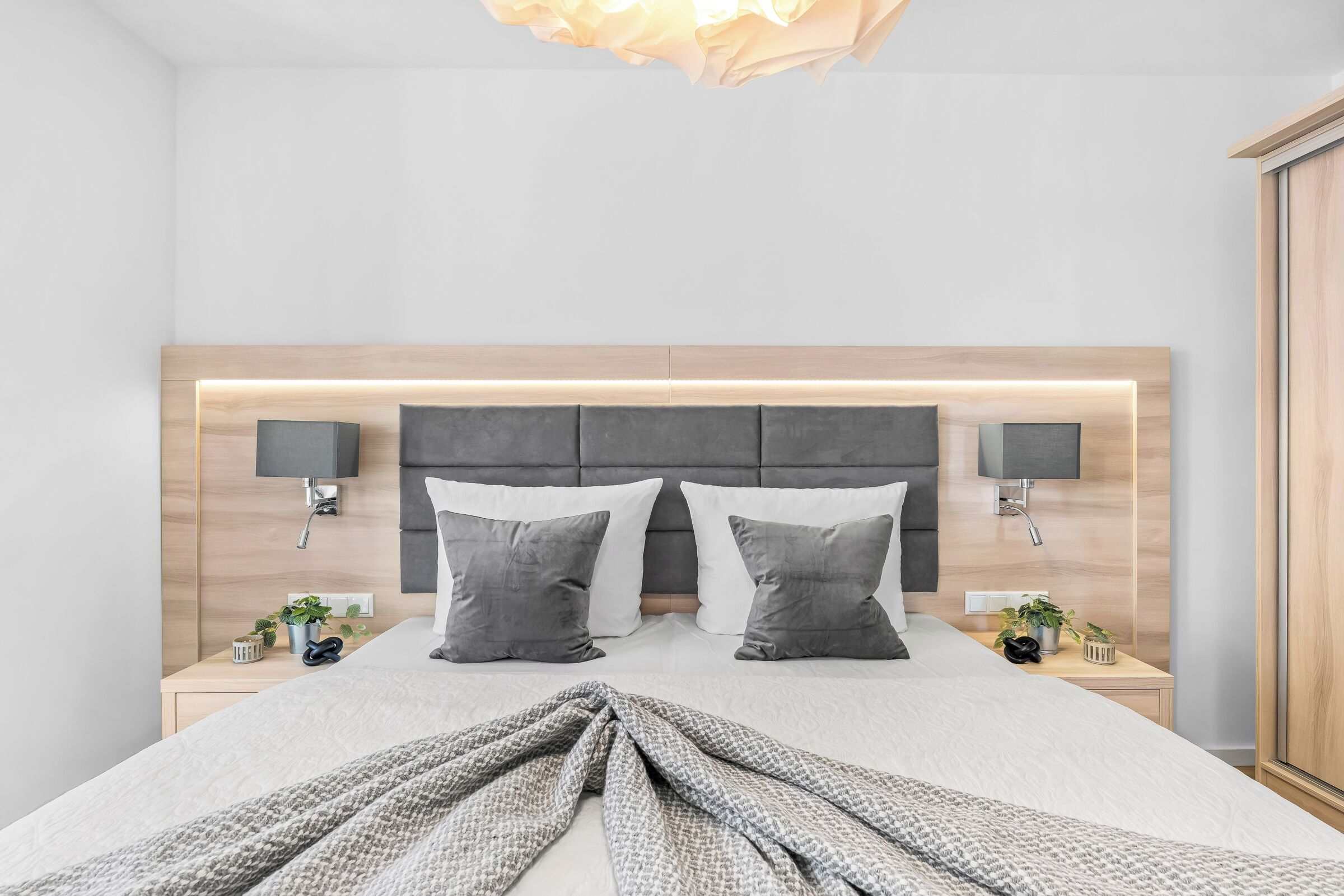 A modern bedroom with a large bed, two bedside tables, a headboard with integrated lighting, and wall-mounted lamps.