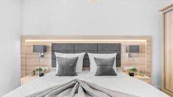 A modern bedroom with a large bed, two bedside tables, a headboard with integrated lighting, and wall-mounted lamps.