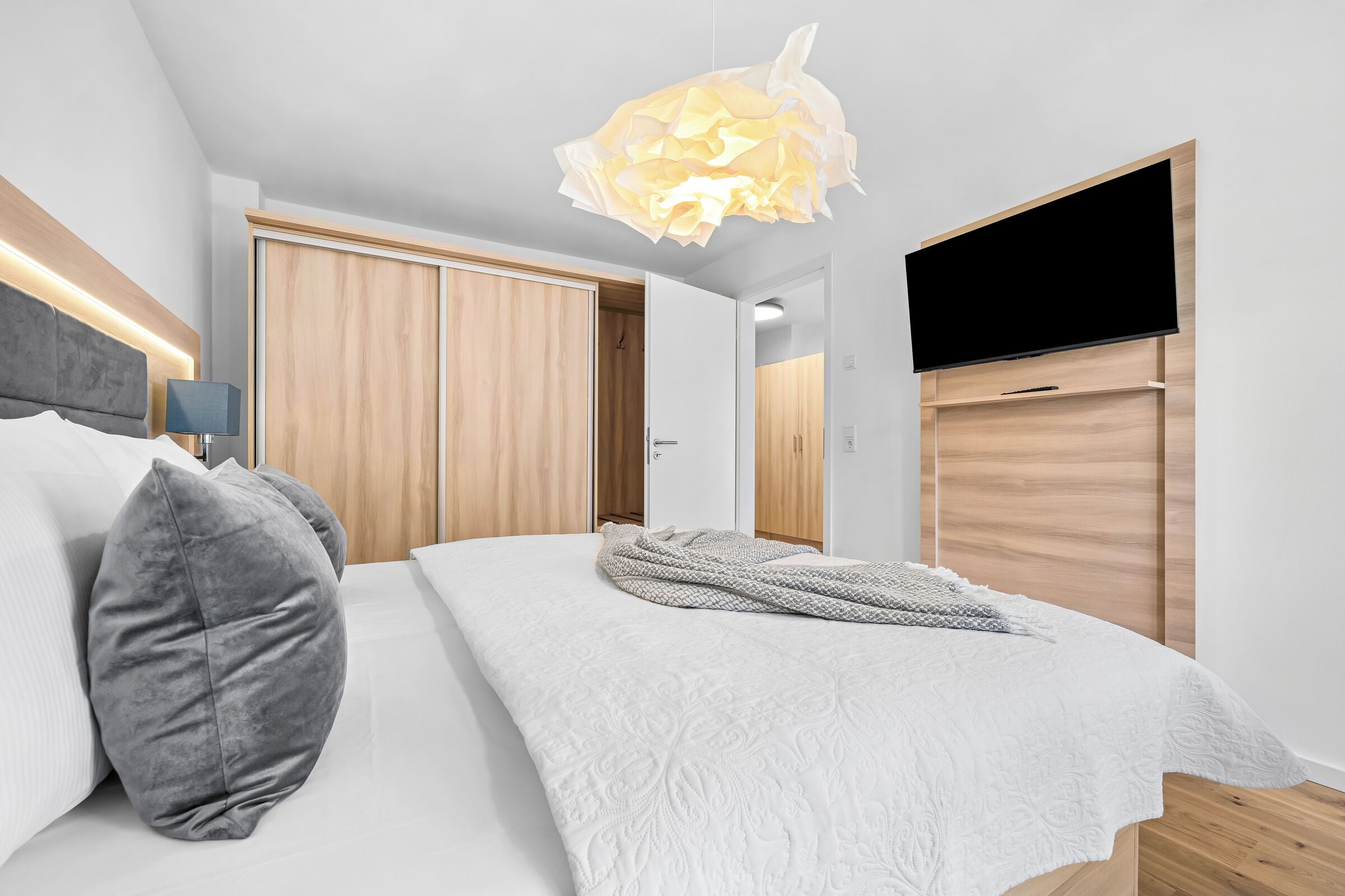 A modern bedroom with a bed, pillows, a TV, and a wardrobe.