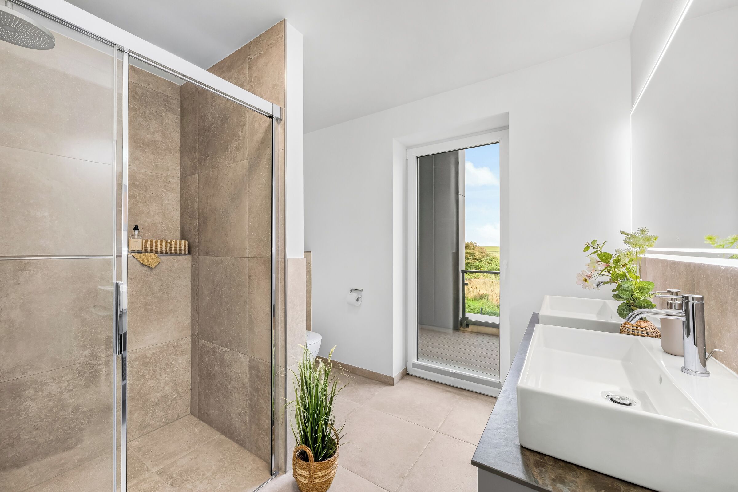Ein modernes Badezimmer mit einer gläsernen Duschkabine, einem großen Spiegel und einem Waschtisch mit zwei Becken.