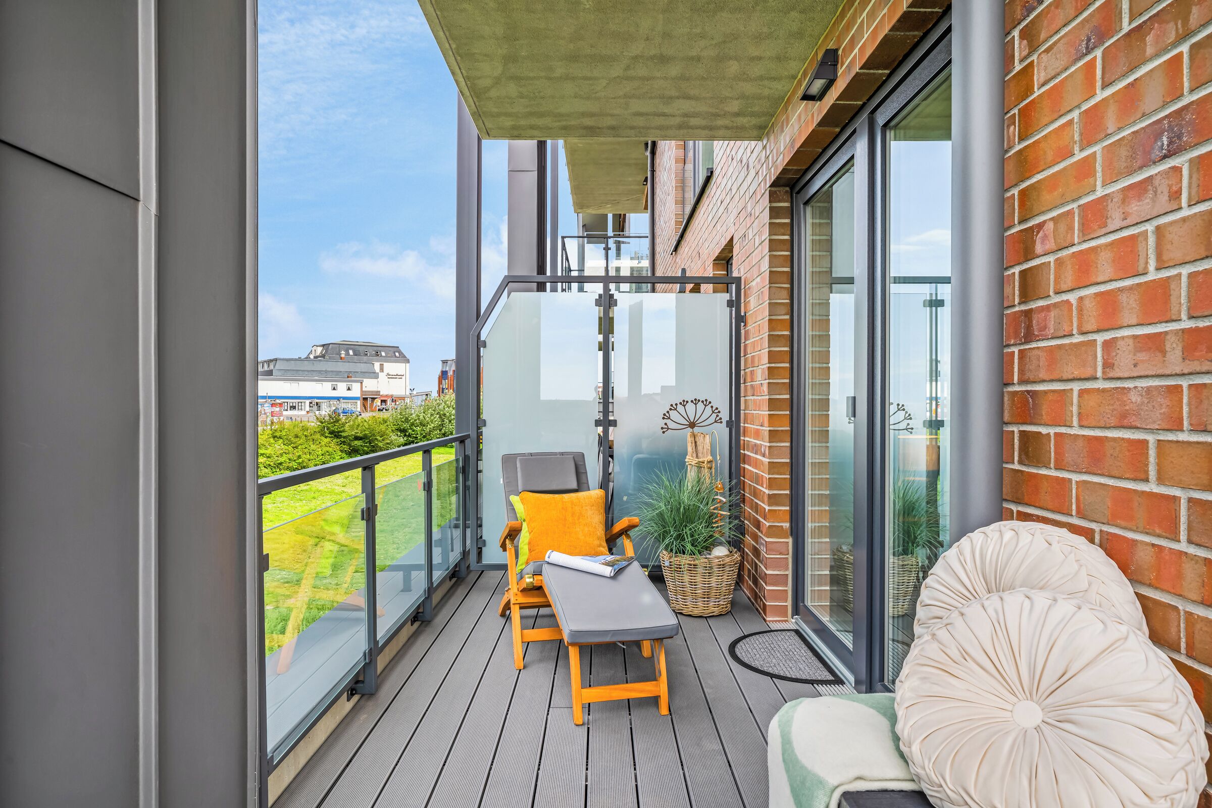 Een balkon met een houten vloer, een grijze bank, een gele stoel en een rieten mand.