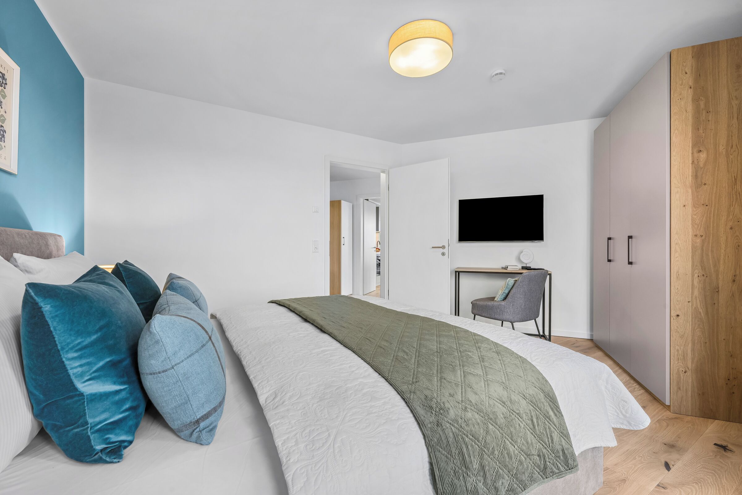Ein modernes Schlafzimmer mit Bett, Kissen, Fernseher und Kleiderschrank.
