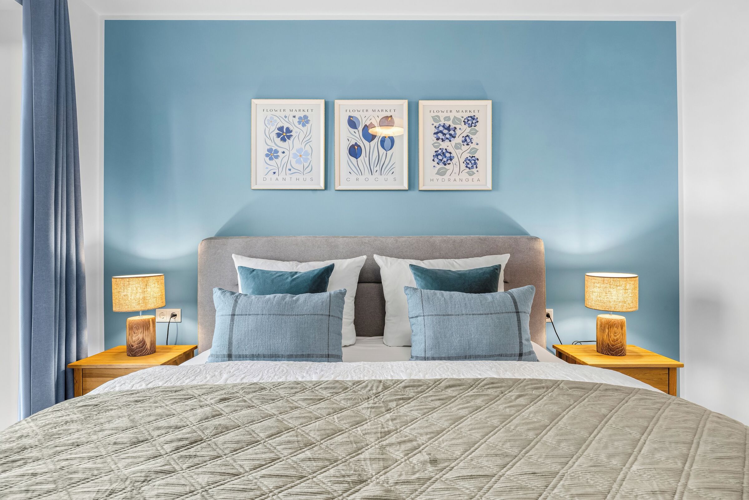 A bedroom with a bed, two bedside tables, a headboard, and three wall-mounted artworks.