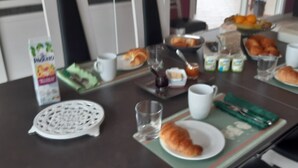 Una mesa de desayuno con croissants, una taza de café, un zumo envasado y un bol de fruta.