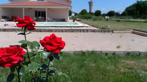 Una casa con piscina, un jardín de rosas y una torre al fondo.