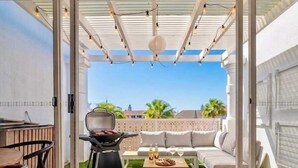 Eine Terrasse im Freien mit Grill, einer Couch und einem Esstisch.