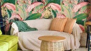 Ein gemütliches Zimmer mit einer Couch, einem runden Weidenbeistelltisch und lebhaftem tropischen Wandpapier.