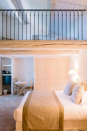 A hotel room with a bed, a desk, and a chair. There is a balcony with a railing.