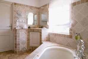 A bathroom with a bathtub, a vanity with a mirror, and a window.