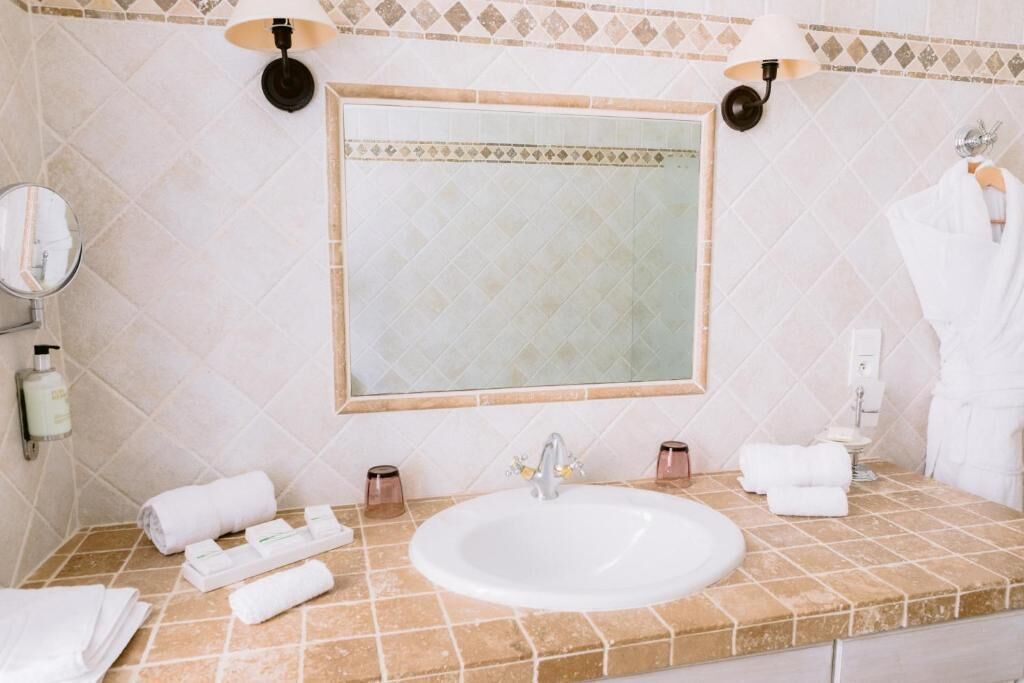 Un baño con un lavamanos blanco, dos luces empotradas en la pared, un espejo grande y un perchero con toallas blancas.
