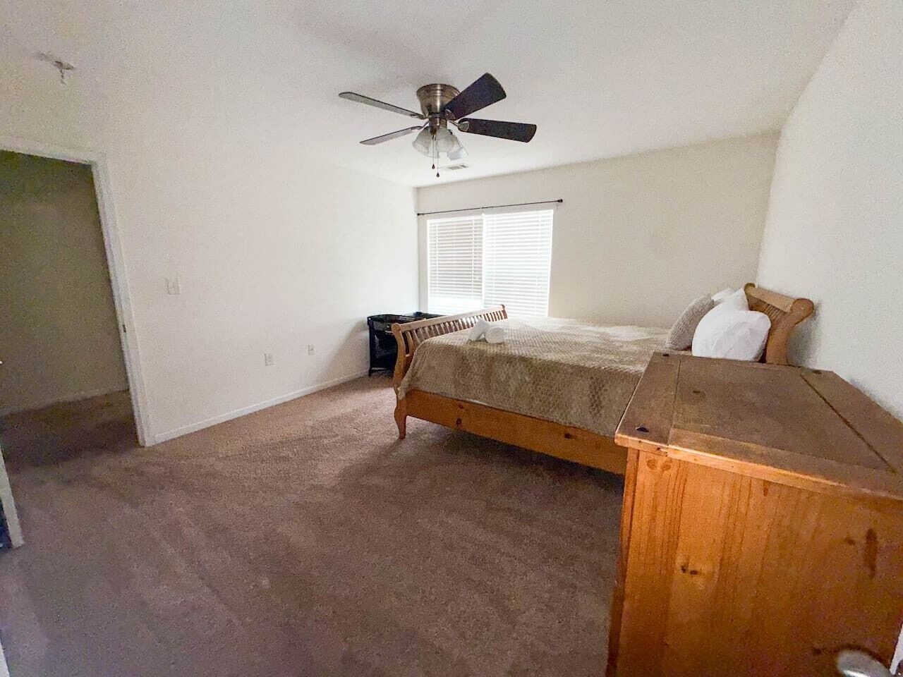 Ein Schlafzimmer mit einem Einzelbett, einem Nachttisch aus Holz, einem Deckenventilator und einem Fenster mit Jalousien.
