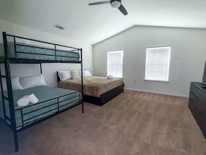 Ein Zimmer mit Etagenbetten, Deckenventilator, zwei Fenstern mit Jalousien und einem Schminktisch.