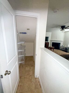 A narrow hallway with a white door on the left, leading to a room with a ceiling fan and a fireplace. - Modern 4BR Near Uptown Charlotte (Charlotte)