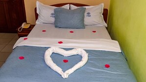 A hotel room with a bed, a wooden headboard, a bedside table with a phone, and a green wall. - hotel le printemps (Douala)