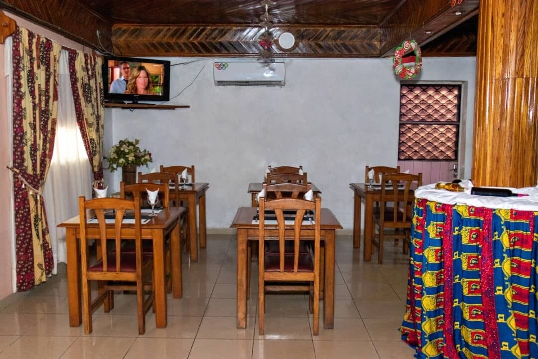 Un'area pranzo con tavoli e sedie in legno, una televisione montata a parete e un condizionatore d'aria.