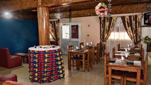 A dining area with wooden tables and chairs, a round table with a colorful tablecloth, and a Christmas wreath hanging from the ceiling. - hotel le printemps (Douala)