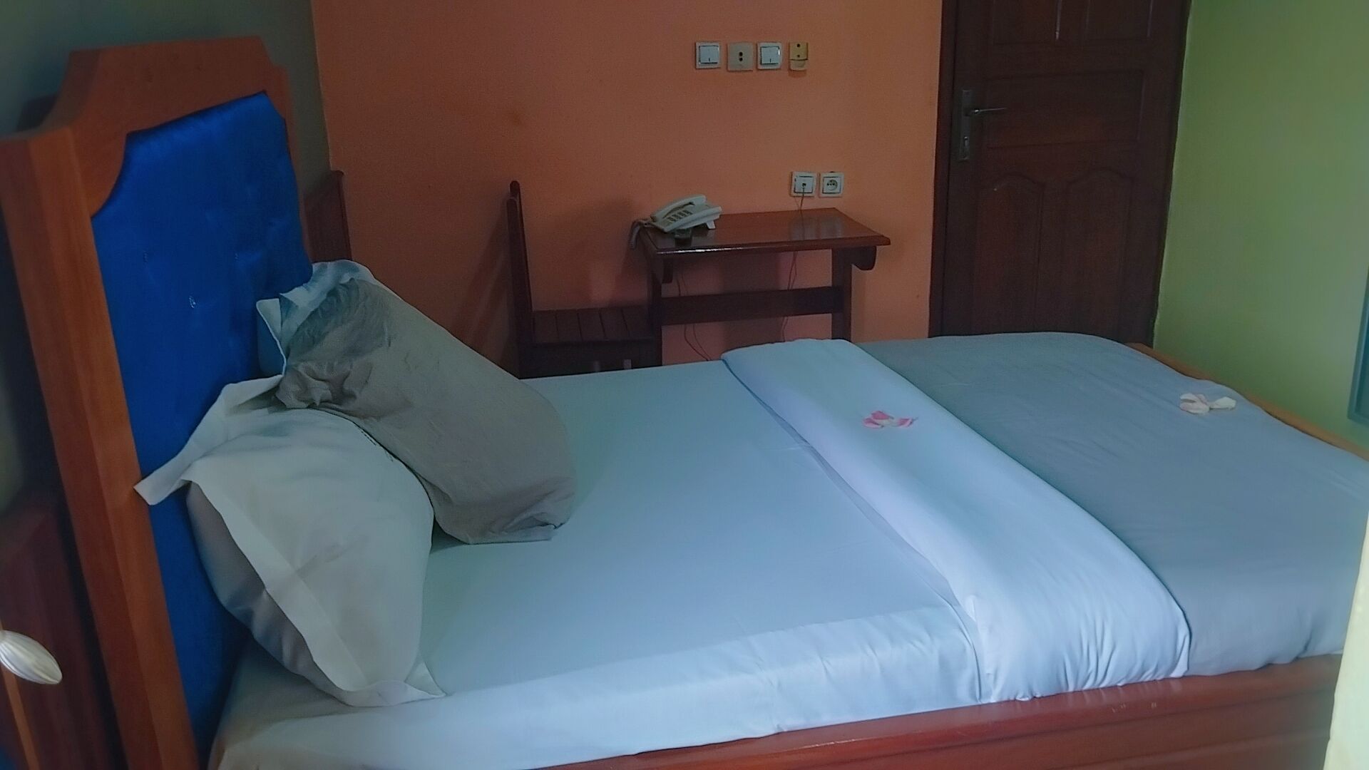 Un llit individual amb capçalera de fusta, una taula de nit amb un telèfon i una presa de corrent.
