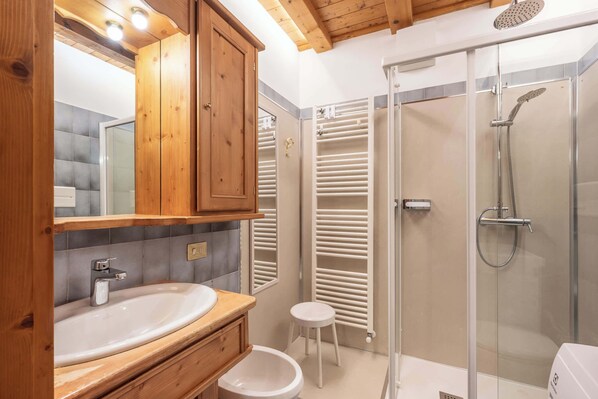 Een moderne badkamer met een houten wastafelmeubel, een douchecabine van glas en een wit toilet.