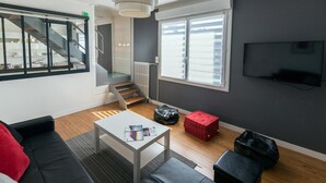 A modern living room with a staircase, a TV, and a window. - Gite Brest at the End of the Pier – One of Fabie’s Gîtes (Brest)