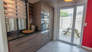 A modern kitchen with built-in appliances, a large window, and a sliding glass door leading to an outdoor area. - Gite Brest at the End of the Pier – One of Fabie’s Gîtes (Brest)