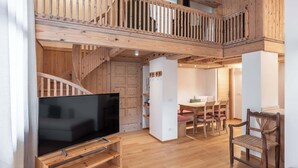 A spacious living area with a wooden staircase, a flat-screen TV on a wooden stand, a dining table with chairs, and a small kitchen area. - Brand new apartment in San Vito di Cadore (San Vito di Cadore)