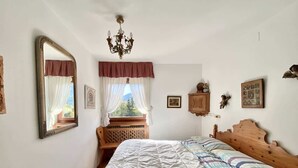 A bedroom with a wooden bed, a large mirror, a chandelier, and a window with curtains. - Charming ground floor flat with mountain views (Cortina d'Ampezzo)