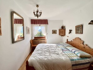 Ein Schlafzimmer mit einem hölzernen Bett, einem großen Spiegel, einer Chandelier und einem Fenster mit Vorhängen.