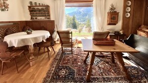 A cozy living room with a wooden dining table, chairs, and a sofa. A large window offers a mountain view. - Charming ground floor flat with mountain views (Cortina d'Ampezzo)