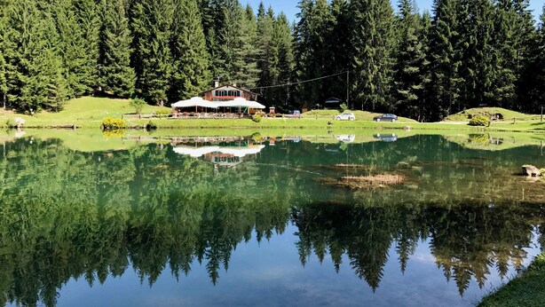 Un lodge sul lago con un grande edificio immerso in una fitta foresta, il suo riflesso limpido nell'acqua e un piccolo pontile con barche.