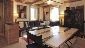 Una sala de estar acogedora con techo de madera, un sofá grande, una mesa de comedor y un aparador con objetos decorativos.