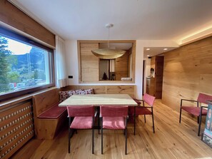Un espace repas moderne avec une table et des chaises en bois, une grande fenêtre donnant sur l’extérieur et un luminaire suspendu.