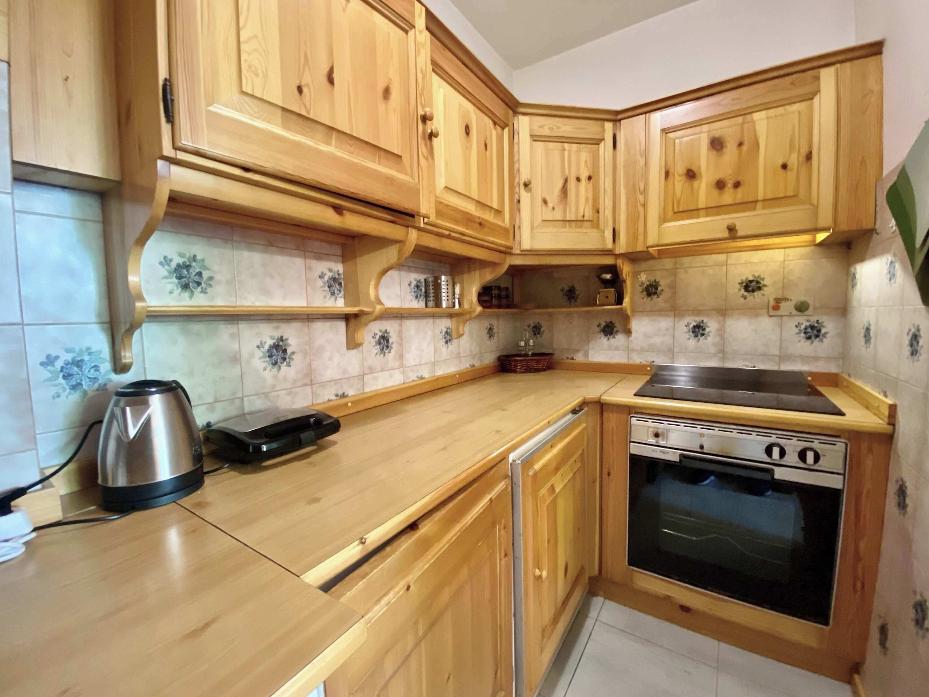 Une cuisine avec des meubles de rangement en bois, une cuisinière et une bouilloire.