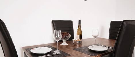A dining table set for four with black chairs, a wine bottle, a bowl of grapes, and a glass of water.