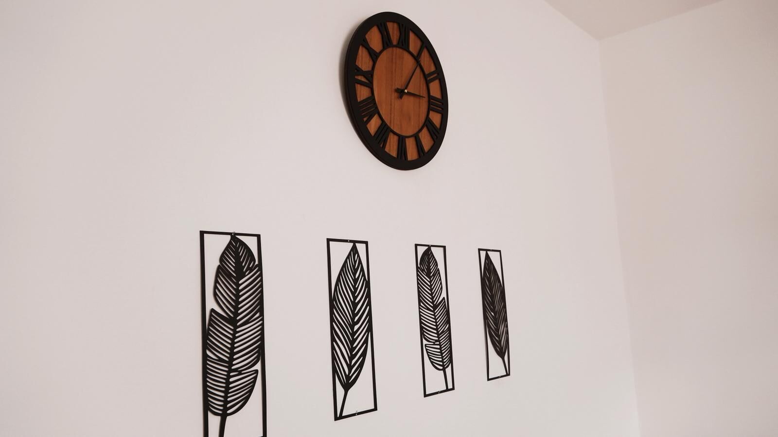 A wall with a wooden clock and four leaf-shaped decorations.