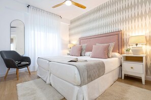 Ein modernes Schlafzimmer mit einem großen Bett, einem Nachttisch mit Lampen, einem Sessel und einer Wand mit Muster.