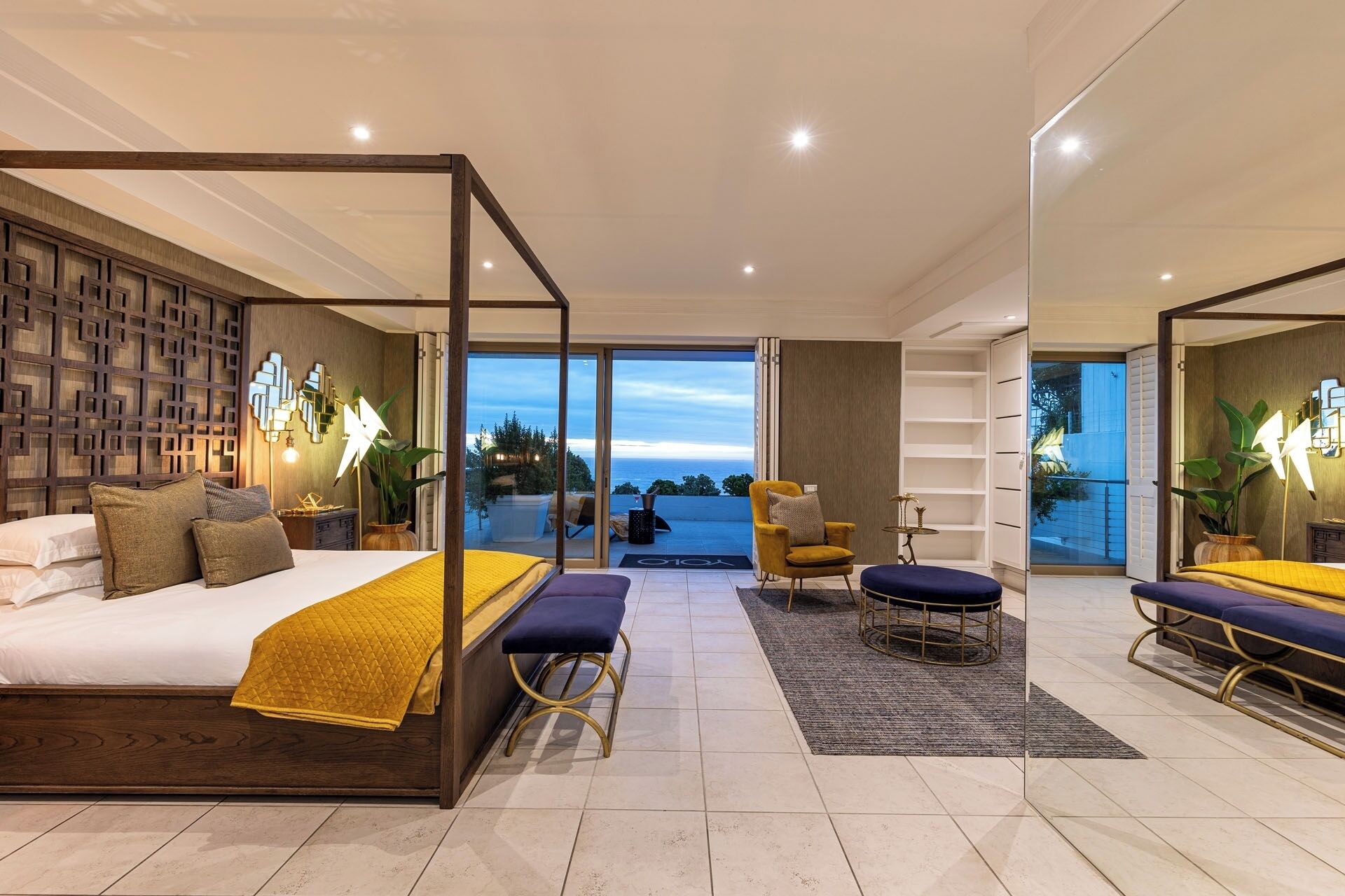 Quarto moderno com cama de dossel, vista para o exterior e varanda com assentos.
