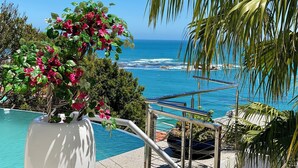 Vista a la piscina con una clara vista al océano, una palmera y un arreglo floral.