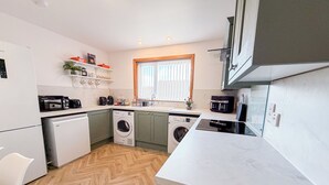 A modern kitchen with a washing machine, microwave, and coffee maker. - Royal Oak Court Retreat (Kirkwall)
