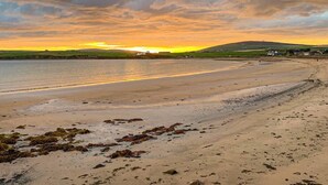 A beach with a sunset, calm water, and distant hills. - Royal Oak Court Retreat (Kirkwall)