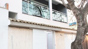 Kaksikerroksinen rakennus, jonka ulkoseinät ovat valkoiset, siinä on lasikaiteilla varustettu parveke ja sen edessä kasvaa puu.
