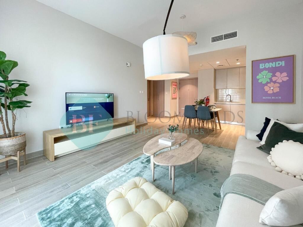 A modern living room with a sofa, a coffee table, and a TV. There is a dining area with chairs and a table in the background.