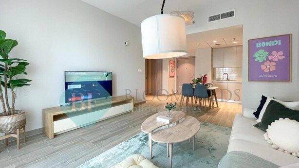 Una sala de estar moderna con un sofá, una mesa de centro y un televisor. Se aprecia un comedor con sillas y una mesa al fondo.