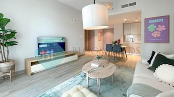 Una sala de estar moderna con un sofá, una mesa de centro y un televisor. Se aprecia un comedor con sillas y una mesa al fondo.