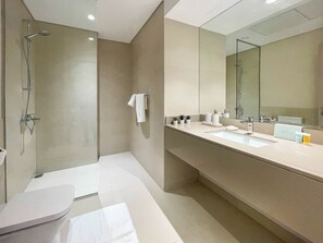 Une salle de bain moderne avec une douche à parois de verre, un grand miroir et un meuble-lavabo avec un évier et des articles de toilette.