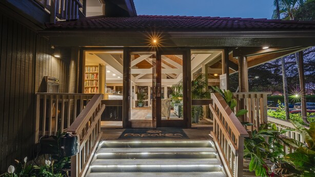 Ein Hotel mit Eingang, einer Holztreppe, einer überdachten Veranda und einem gut beleuchteten Innenraum, der durch die Glastüren sichtbar ist.