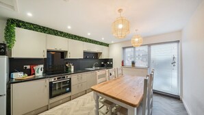 A modern kitchen with white cabinets, a wooden dining table, and pendant lights. - Roll-top bath, rain shower and space for 8 in the heart of Filey (North Yorkshire)