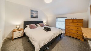 A bedroom with a bed, bedside tables, a dresser, and a ceiling light. - Roll-top bath, rain shower and space for 8 in the heart of Filey (North Yorkshire)